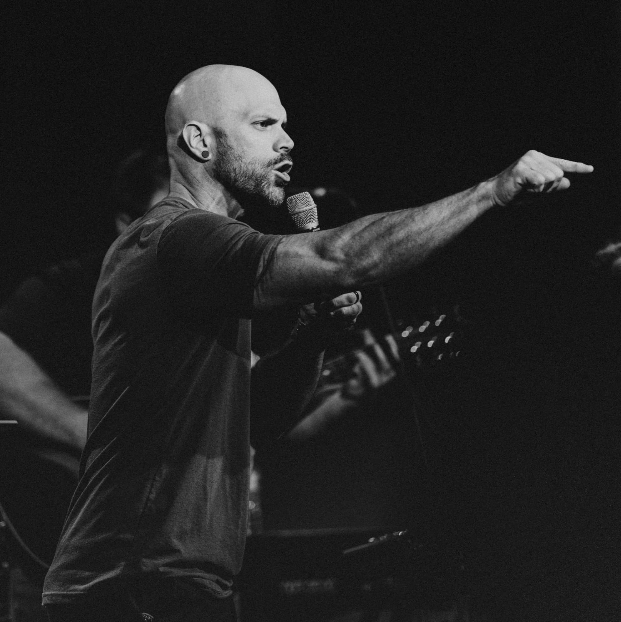 Black and white photo of Aaron Brewer preaching on a stage while pointing a finger off stage
